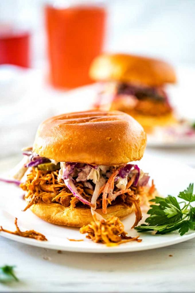 Side photo of two Slow Cooker BBQ Chicken Sandwiches on white plates.