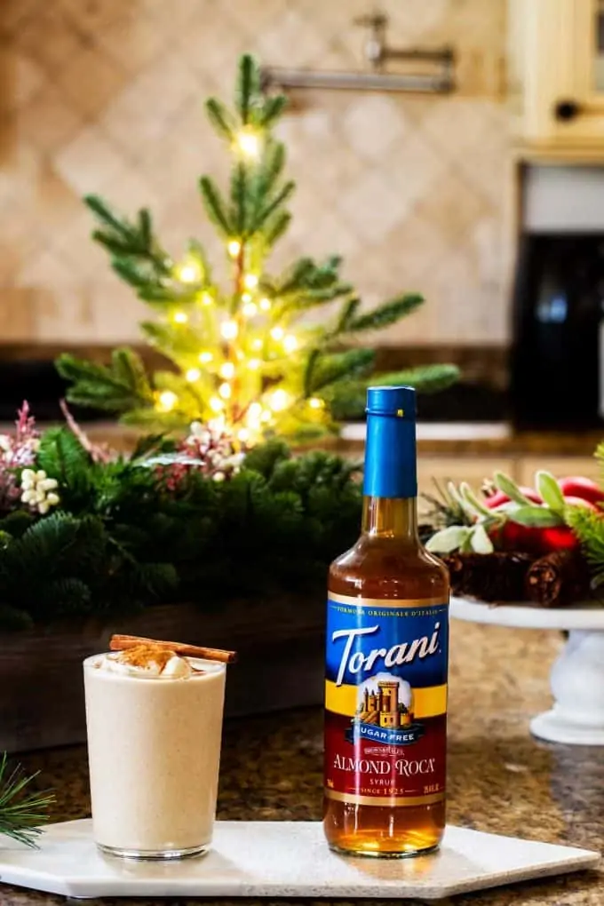 Photo of sugar free eggnog and torani syrup in a kitchen with holiday decorations behind them.