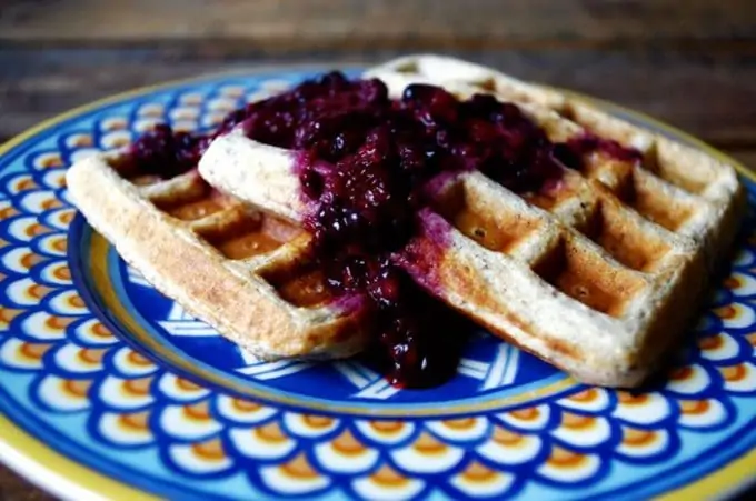 Photo of quinoa waffles on a blue plate with blackberry sauce.