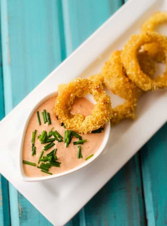Overhead photo of a platter of Healthy Baked Onion Rings with a dipping sauce.