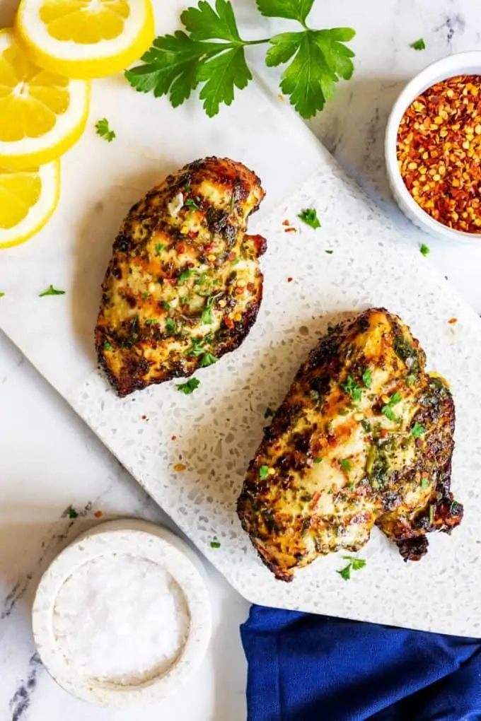 Two pieces of ninja foodi grill chicken on a white marble board garnished with parsley.
