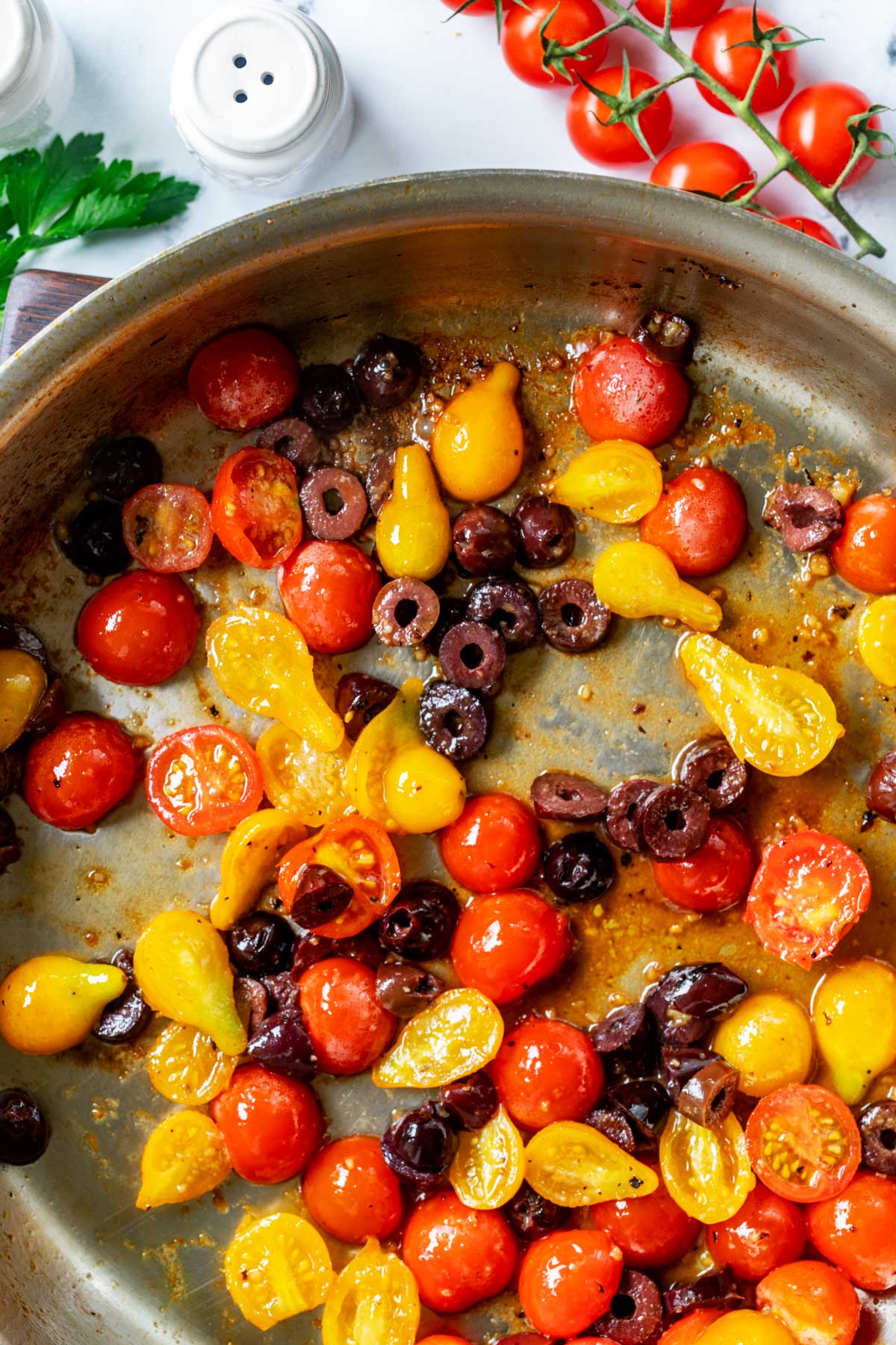 Photo of garlic, broth, tomatoes, and olives in a large skillet.