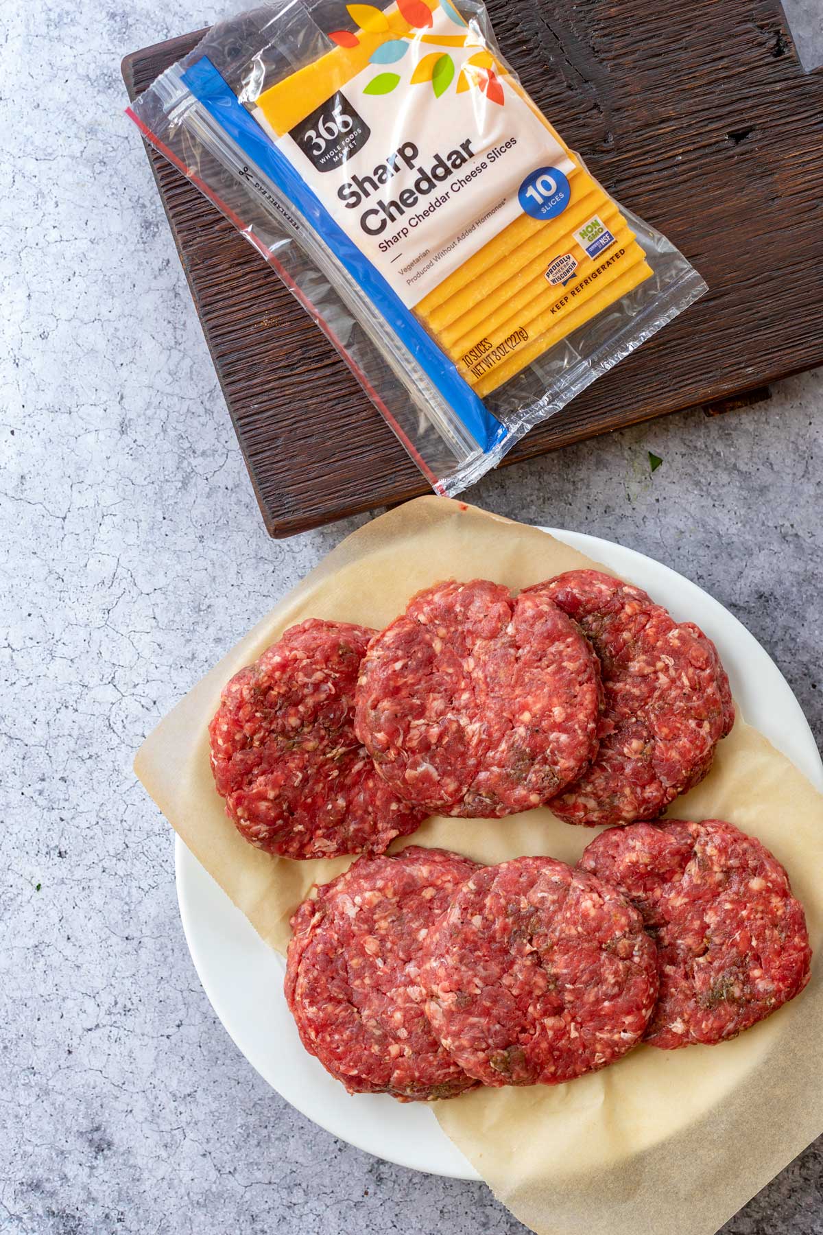Photo of prepared hamburger patties sitting next to a package of sliced sharp cheddar.