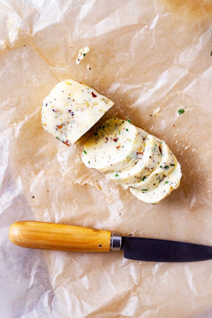 Photo of garlic chive compound butter on parchment paper with a knife next to it.