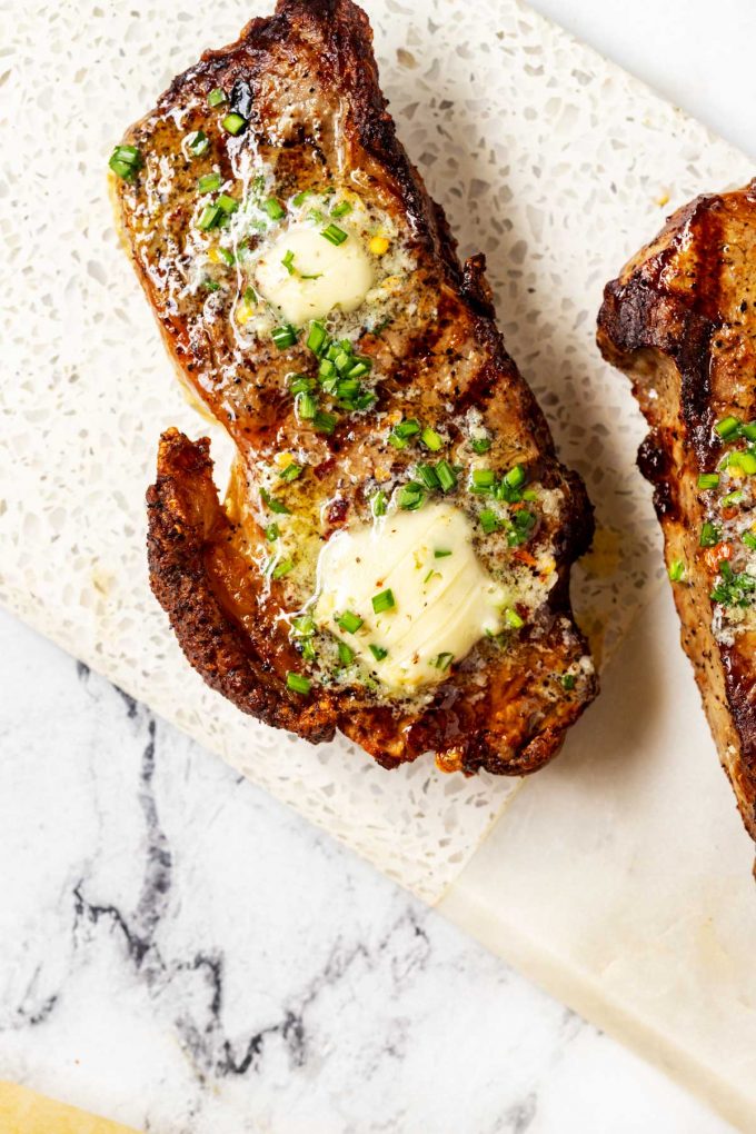 Photo of a strip steak with garlic chive butter melting over it.