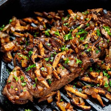 Square photo of steak and mushrooms and onions in a cast iron skillet.