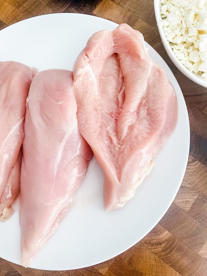 Photo of a plate of raw chicken with a slit cut in it to form a pocket.
