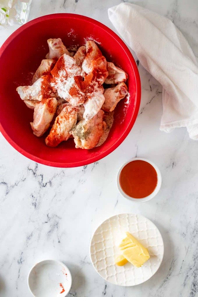 Wings with seasonings on top of them in a large red bowl.