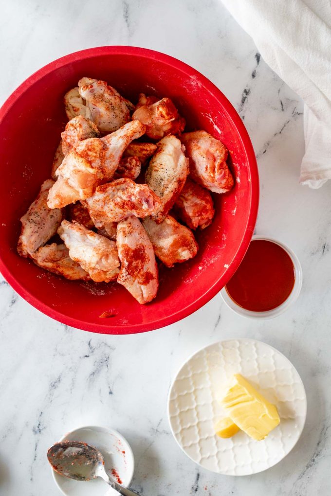 Wings that have been tossed with seasonings in a large red bowl.