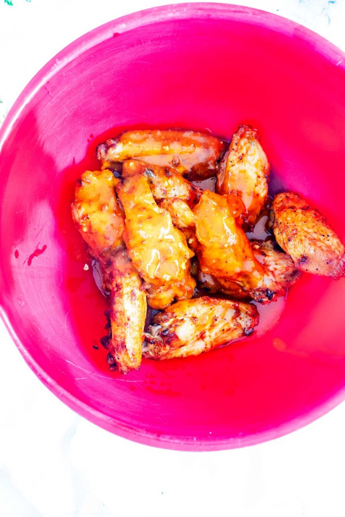 Photo of chicken wings being tossed in buffalo sauce in a red bowl.