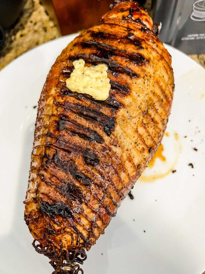 Photo of boneless turkey breast that has been cooked for 30 minutes, removed from the grill and is happing butter rubbed all over it.