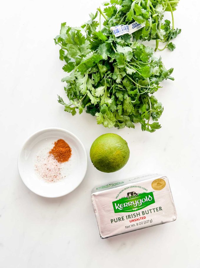 Overhead photo of cilantro, a lime, butter, and seasonings against a white background.