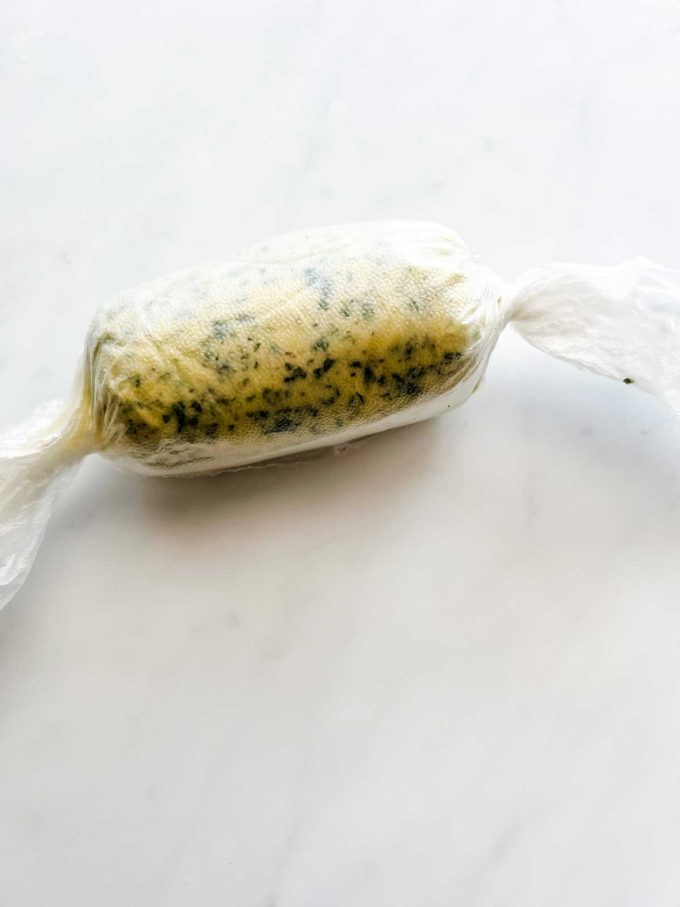 Photo of compound butter that has been just made and rolled up in plastic wrap.