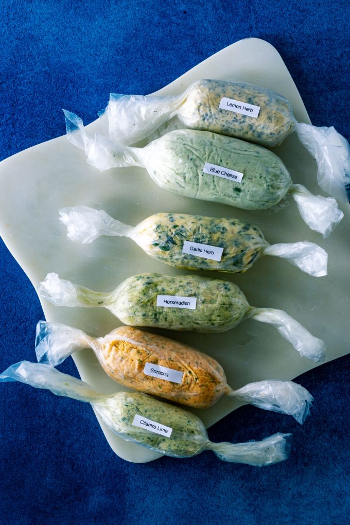 Overhead photo of six kinds of compound butter wrapped in plastic wrap and labeled.