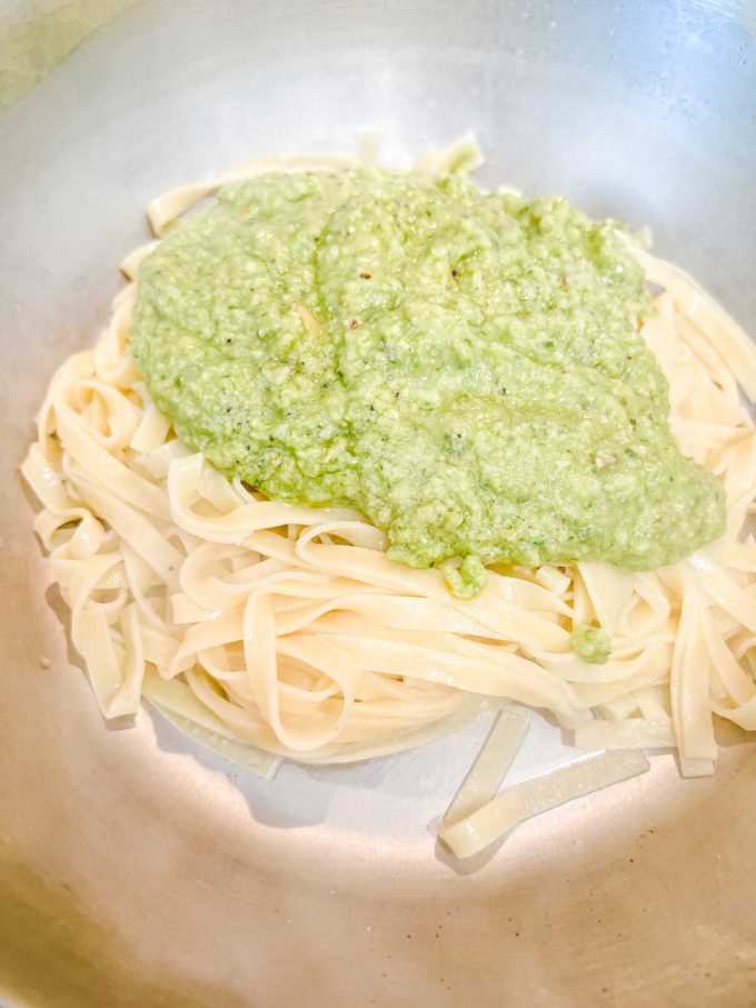 Photo of cooked pasta with avocado pesto on top of it.