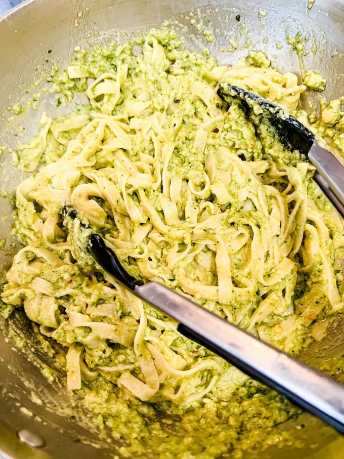 Photo of cooked pasta being tossed with avocado pesto.