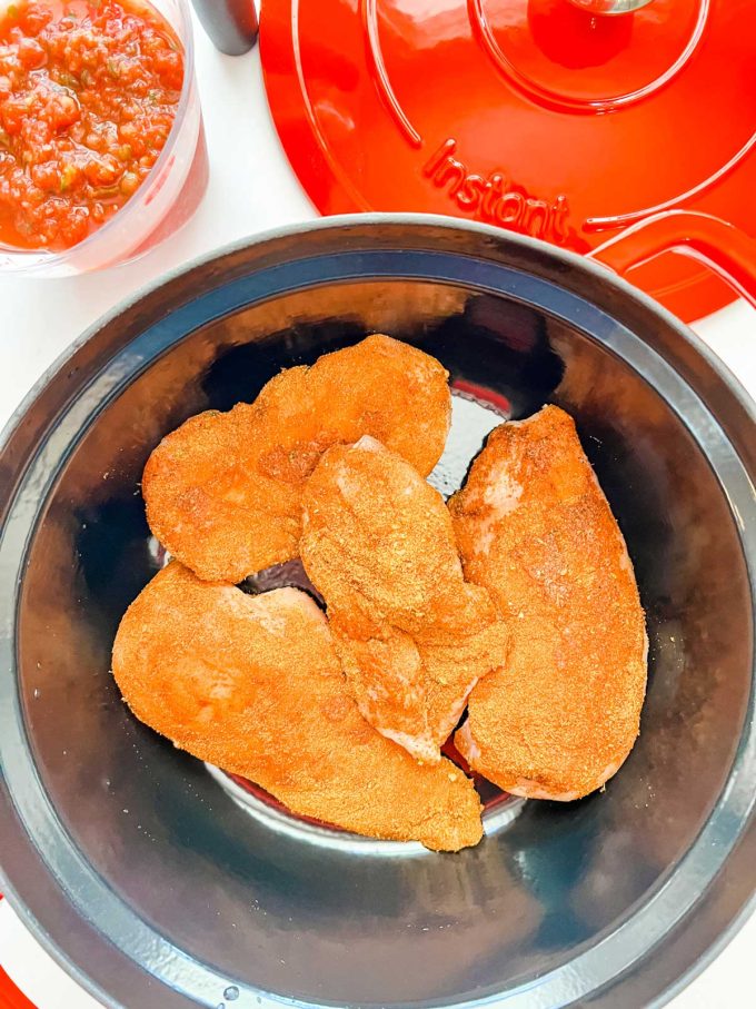 Photo of seasoned chicken in an Instant Pot Dutch Oven with a container of salsa next to it.