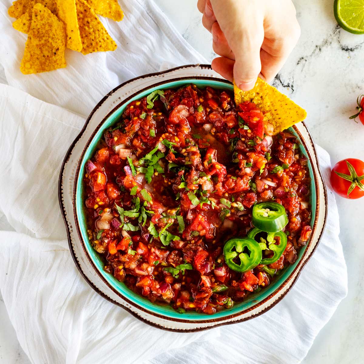Square overhead photo of a bowl of homemade chipotle salsa that someone is scooping a bite from with a tortilla.