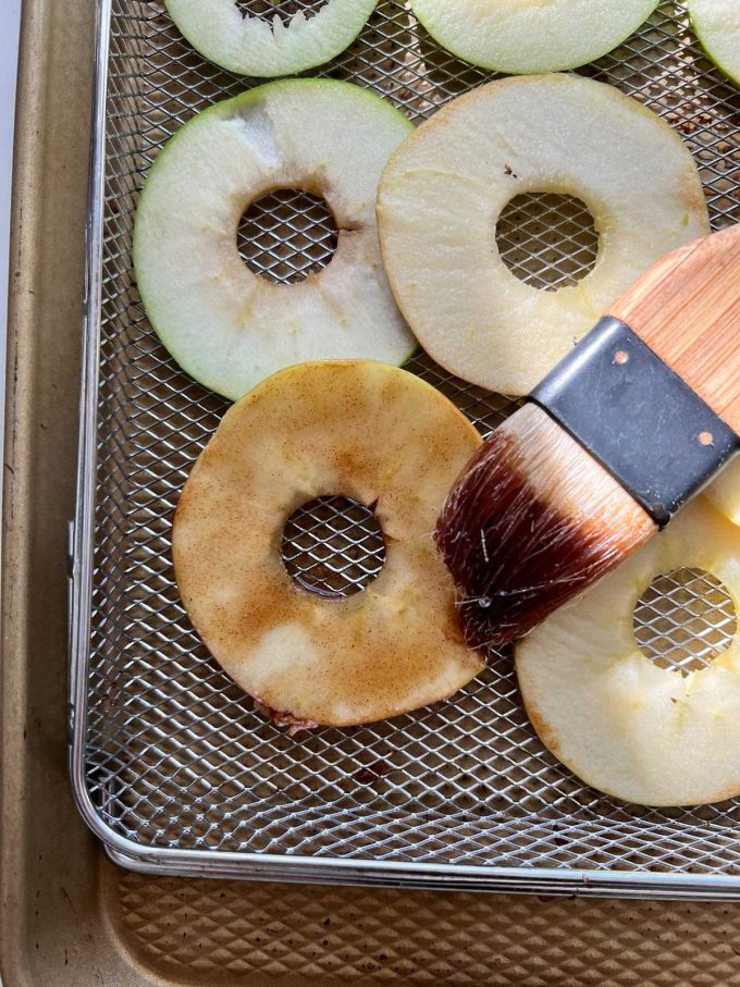 Photo of thinly sliced apples with a maple syrup glaze being brushed onto them.