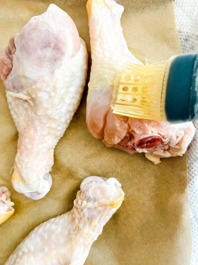 Chicken drumsticks being brushed with oil.