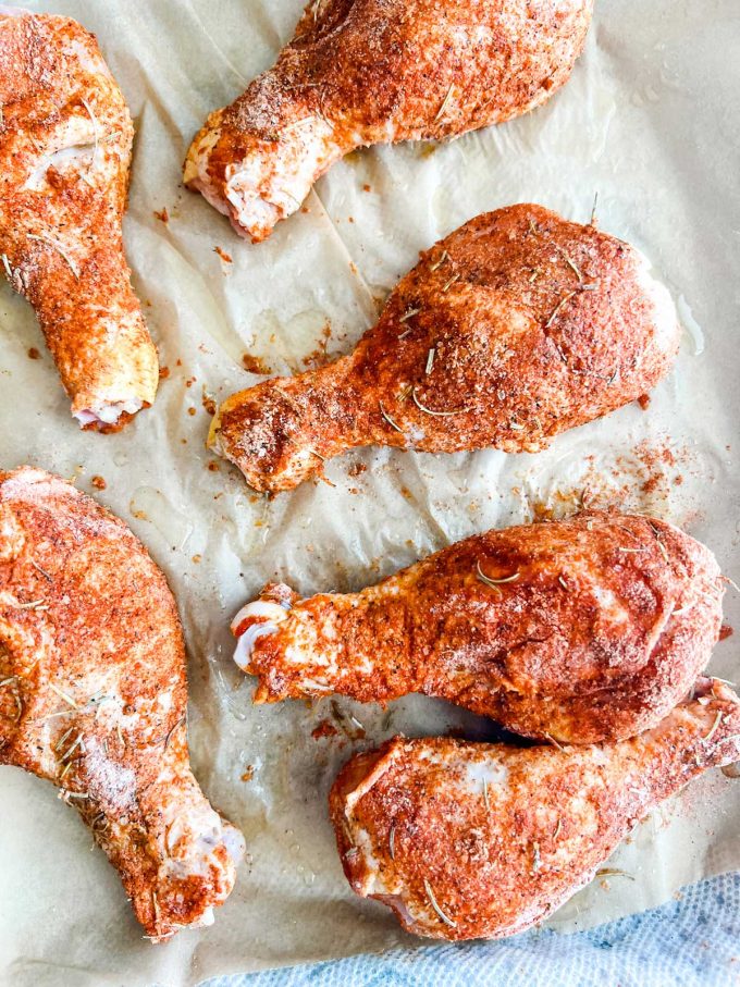 Parchment lined baking sheet with seasoned chicken legs.