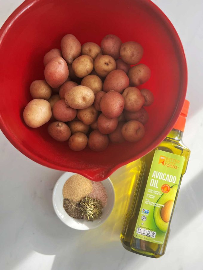 Overhead photo of a bowl of potatoes, avocado oil, and seasonings.