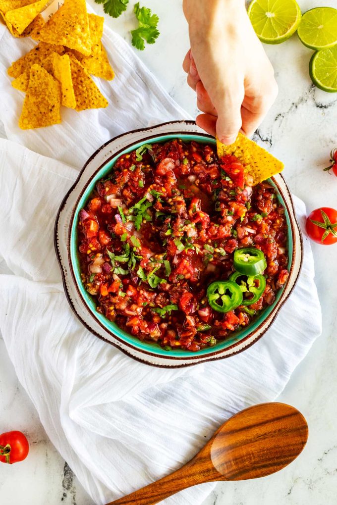 Overhead photo of a bowl of homemade chipotle salsa that someone is scooping a bite from with a tortilla.