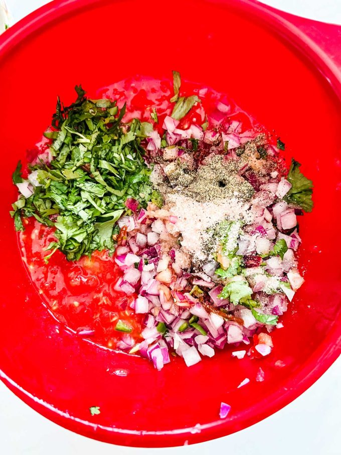 Photo of chopped tomatoes, onion, chipotle chiles, jalapeno, garlic, lime, cilantro, salt and pepper in a large bowl.