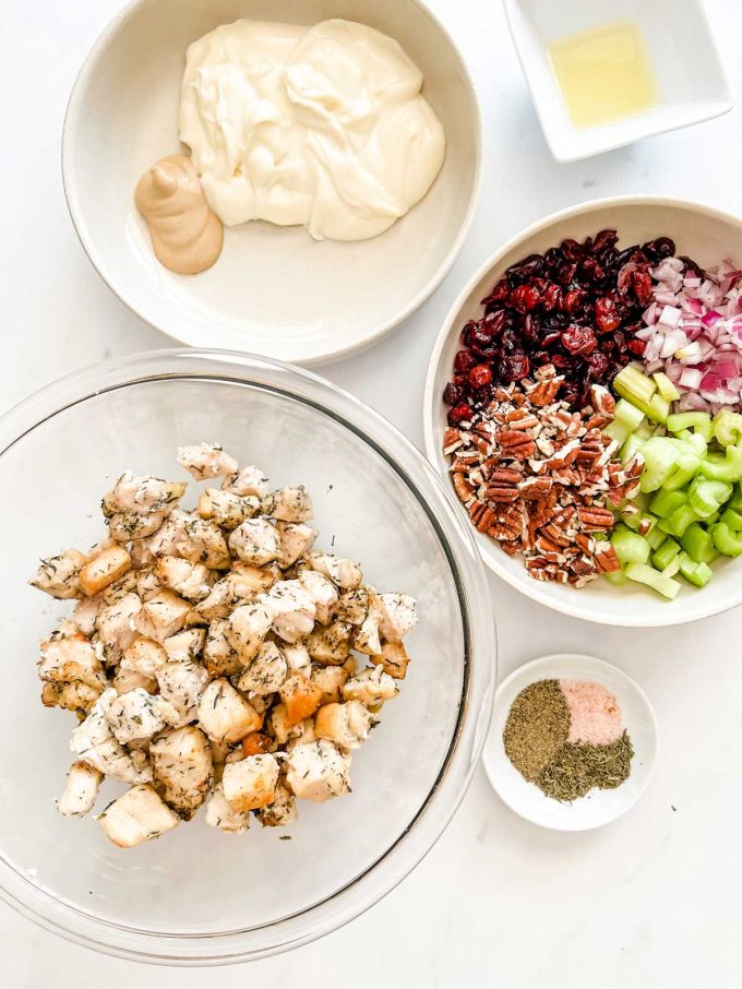 Overhead photo of prep bowls with chicken, seasonings, cranberries, pecans, red onion, celery, lemon juice, mayonnaise, and dijon mustard.