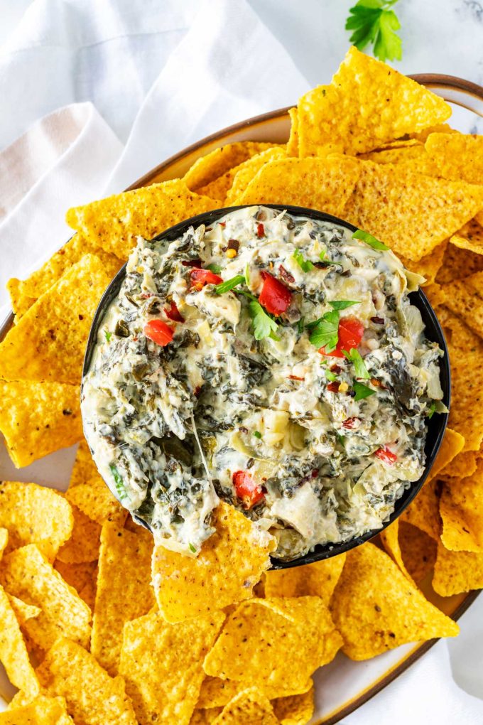 Photo of crockpot spinach artichoke dip on a platter surrounded by tortilla chips.