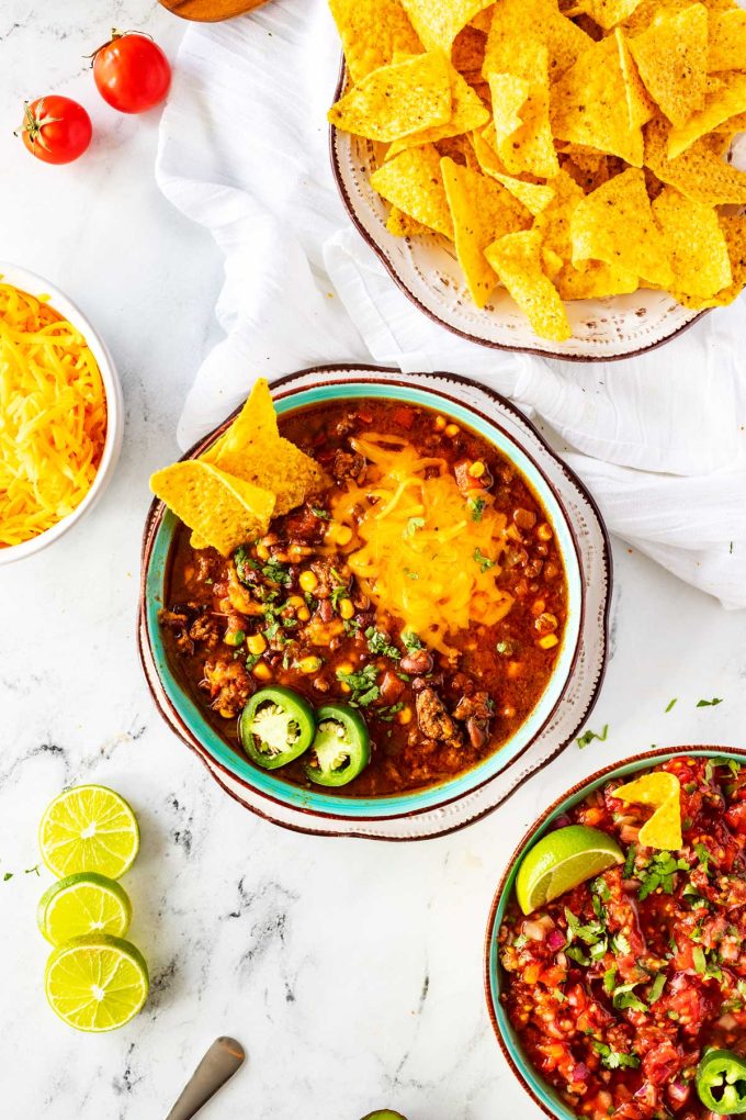 Overhead photo of crockpot taco soup in a blue bowls surrounded by chips, cheese, and salsa.