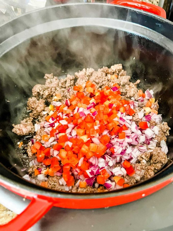 Photo of browned ground beef with red pepper and red onion that has been added to it.
