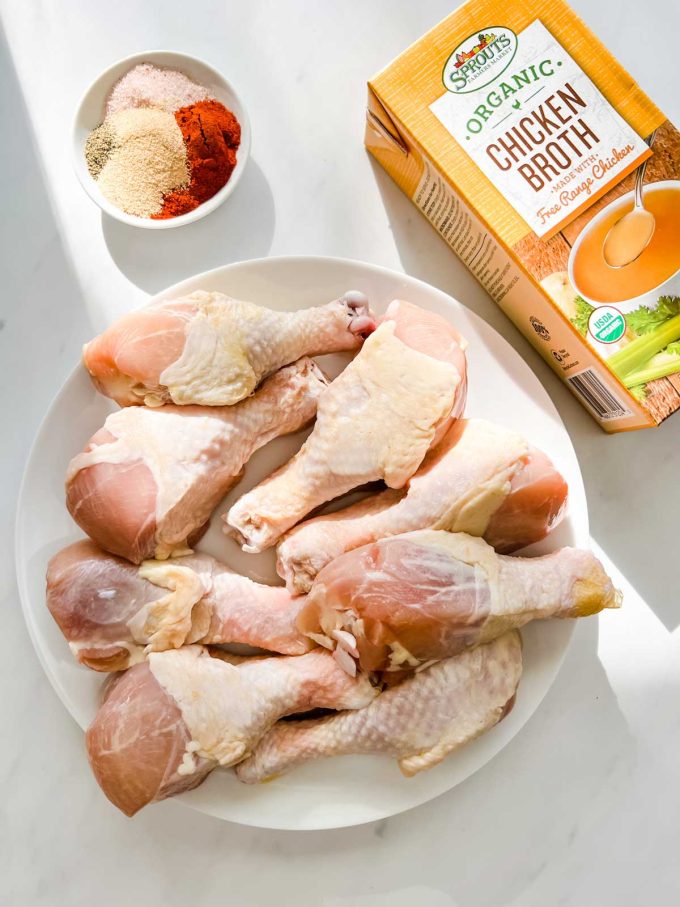 Overhead photo of chicken drumsticks on a plate, chicken broth, and seasonings.
