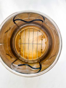 Overhead photo of an instant pot with chicken broth with a trivet on top of it.