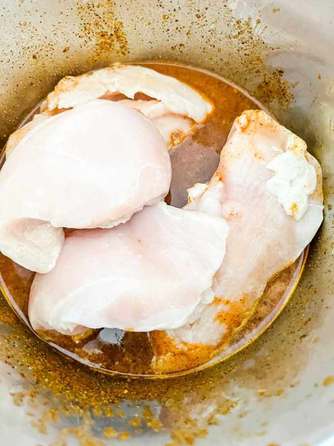 Photo of chicken on top of broth and seasonings in an Instant Pot.