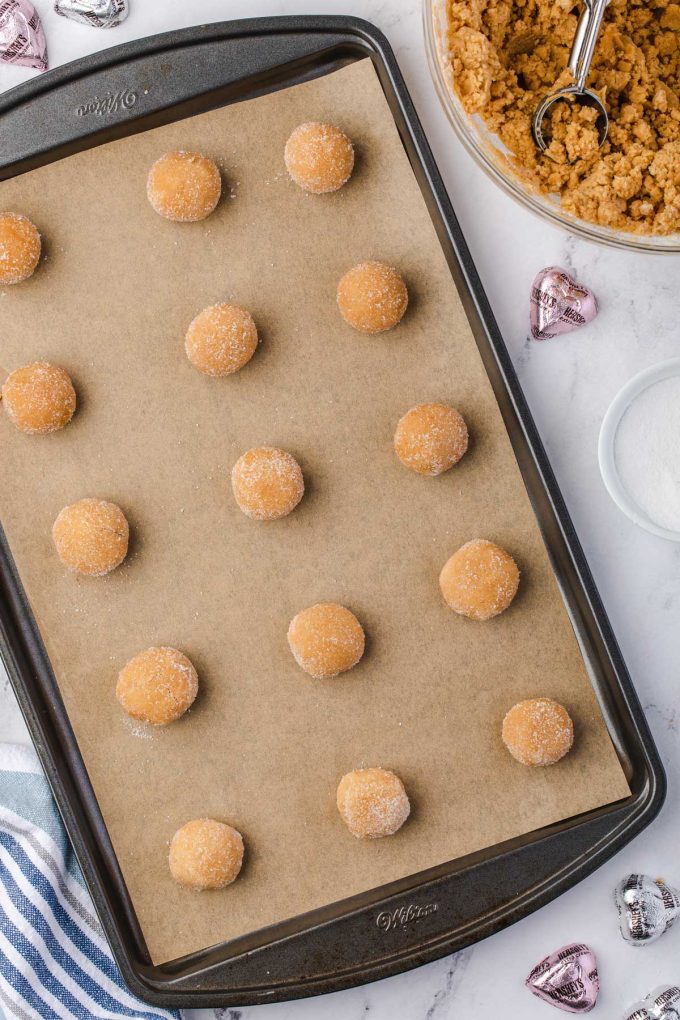 Photo of uncooked peanut butter blossoms in balls on a parchment lined baking sheet.