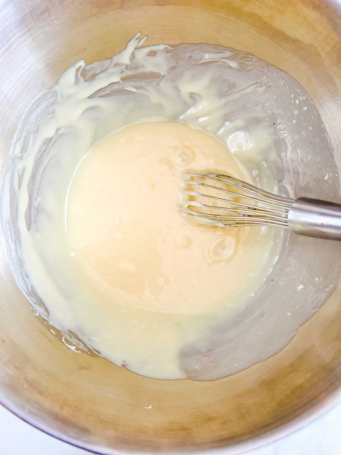 Photo of white chocolate, butter, and heavy cream being whisked together.