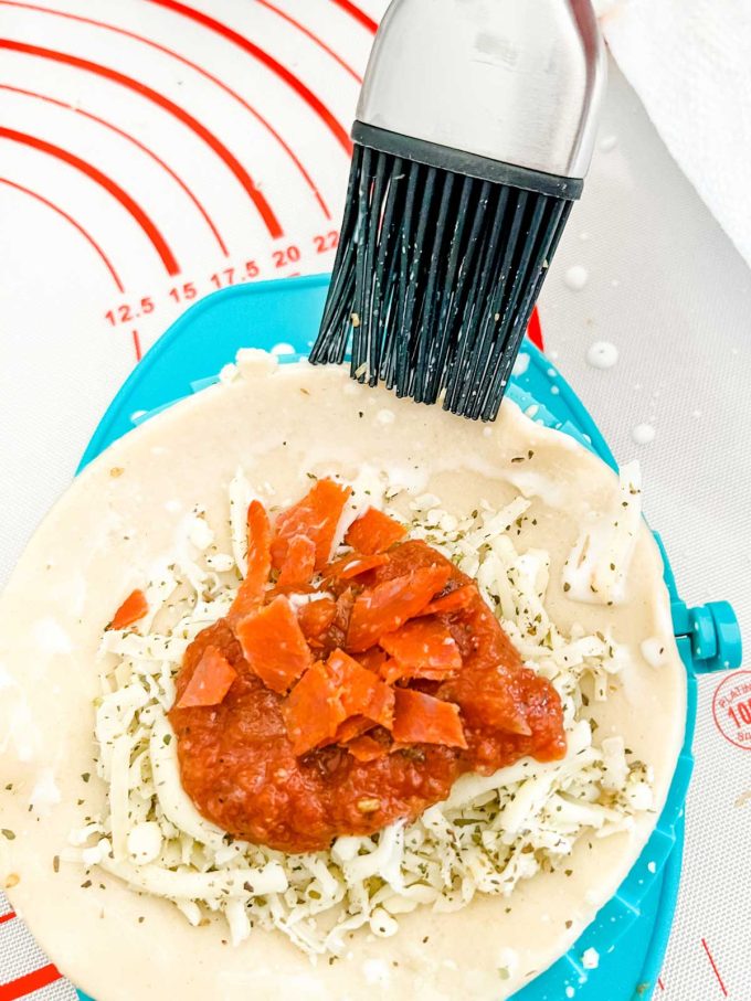 Photo of milk being brushed on the edges of an air fryer pizza pocket.