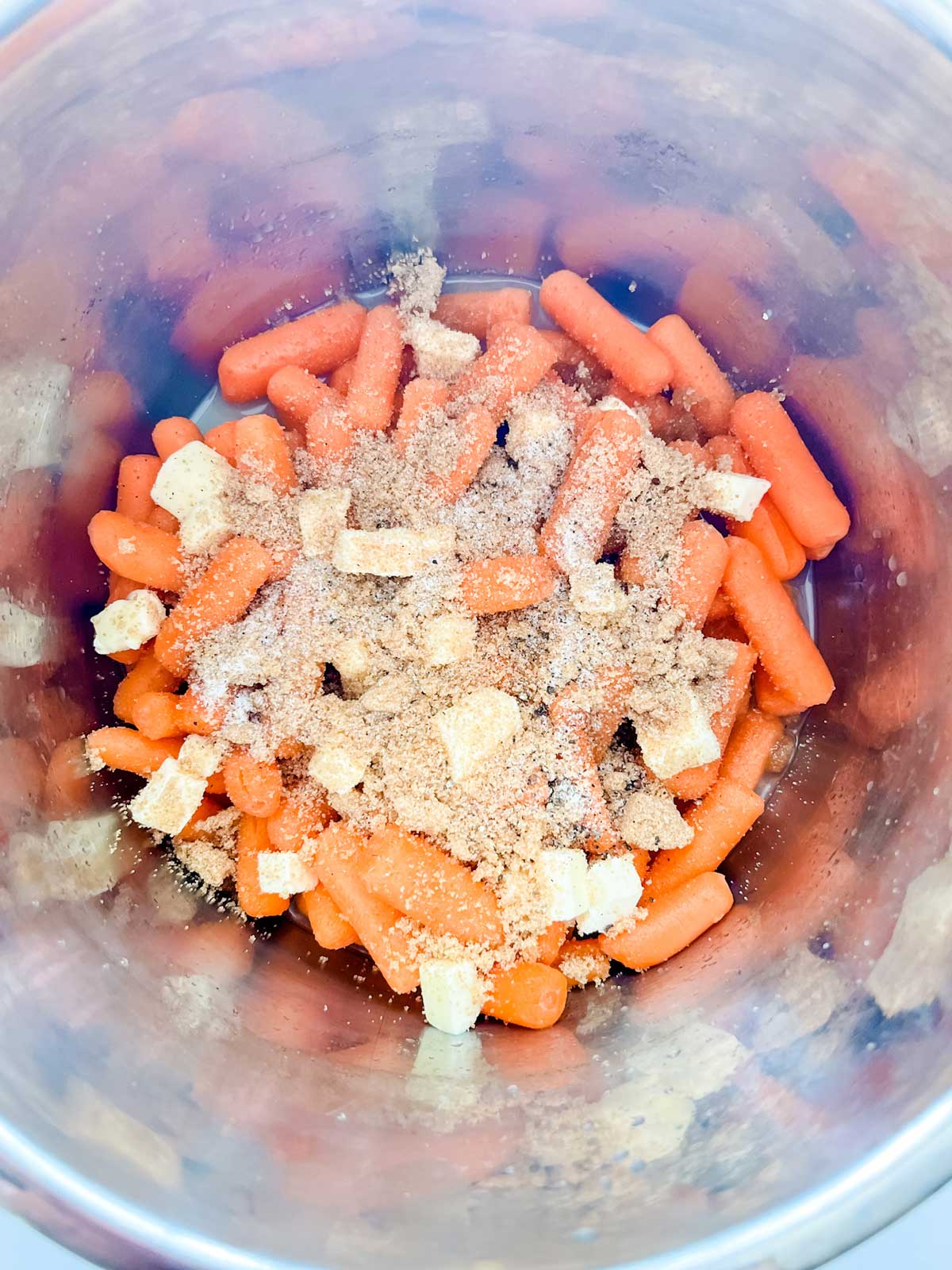Photo of brown sugar and seasonings over butter, carrots, and broth in an Instant Pot.
