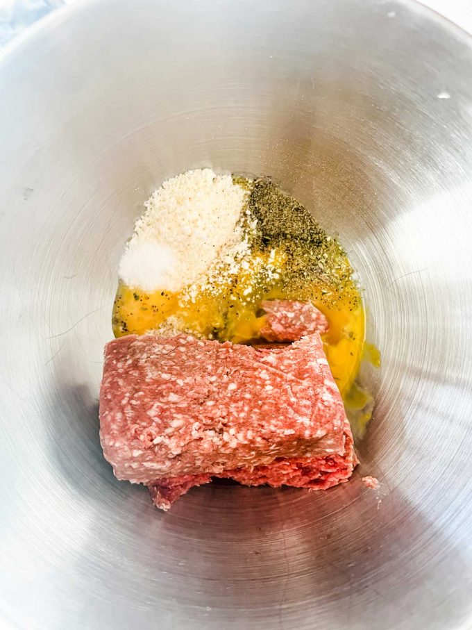 Photo of ground beef, eggs, parmesan and seasonings in a metal bowl.