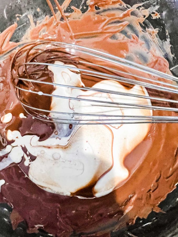 Photo of heavy cream being poured into melted chocolate and coconut oil.