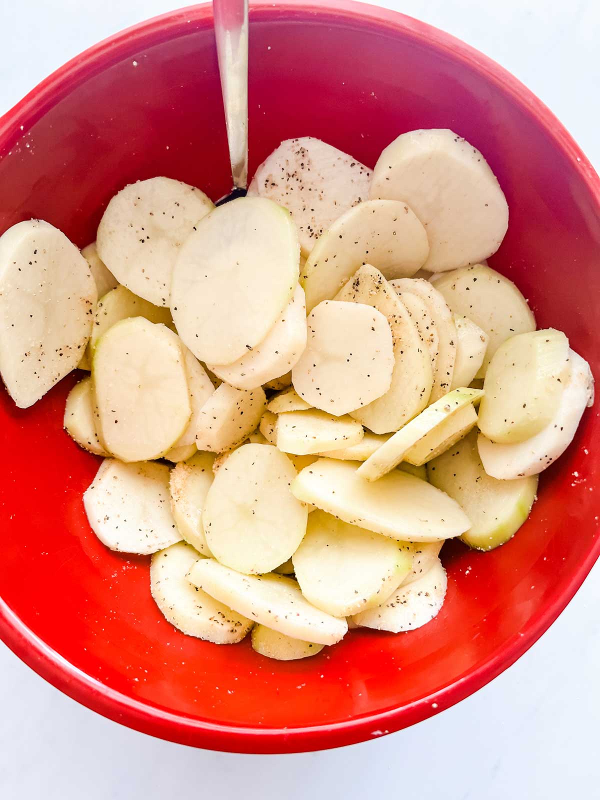 Photo of a red bowl with potatoes that have been tossed in seasonings.