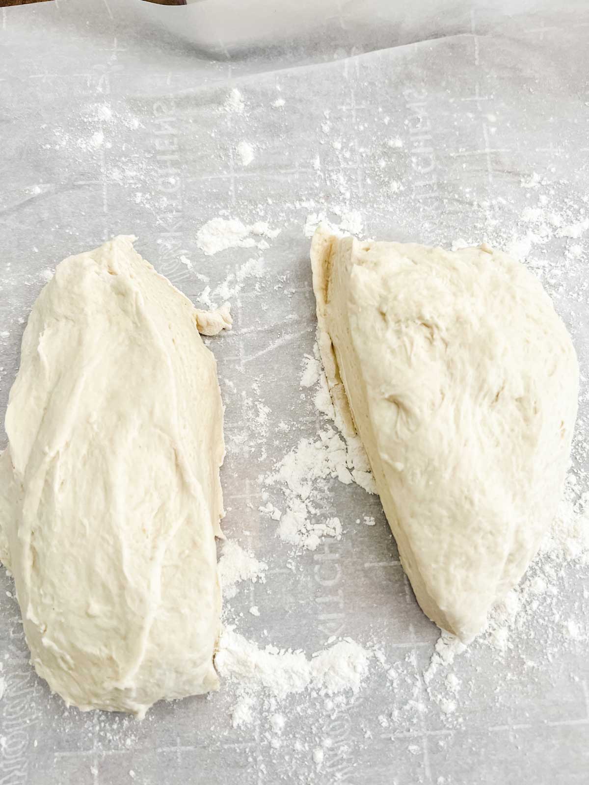 Pizza dough that has been cut in half on a flour lined piece of parchment paper.