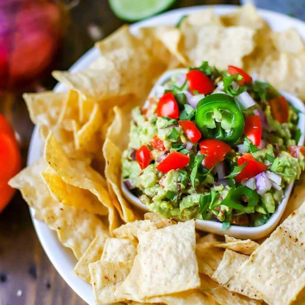 Square photo of a dish of guacamole on a platter surrounded by tortilla chips.