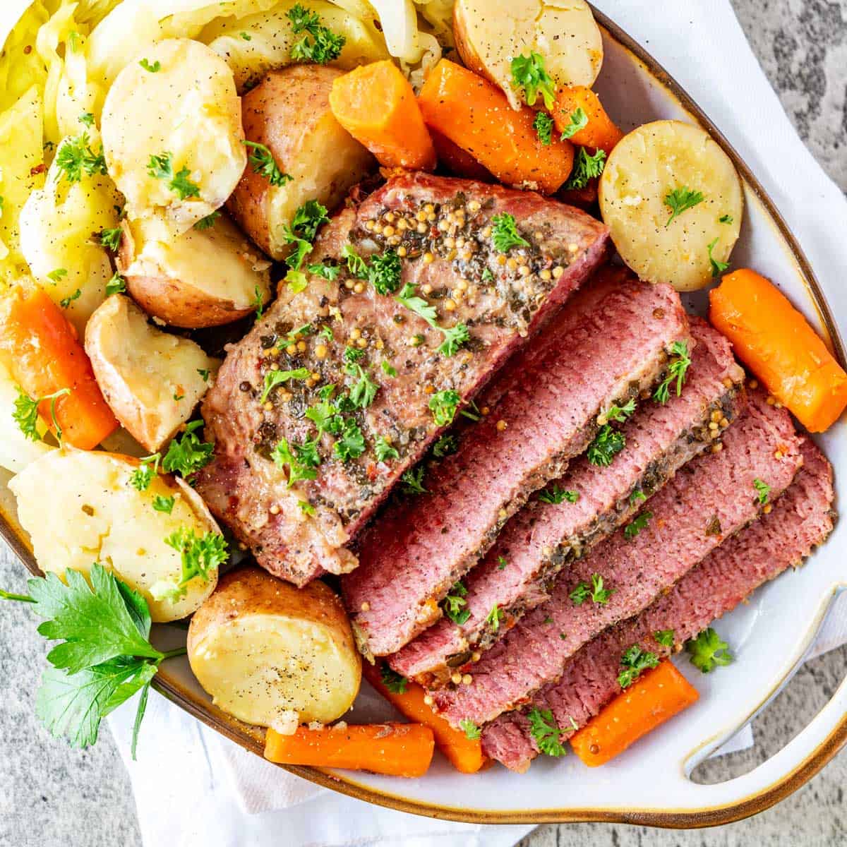Square overhead photo of a platter of Dutch Oven Corned Beef and Cabbage with potatoes and carrots garnished with parsley.