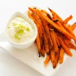 Square photo of cashew lime crema garnished with lime zest sitting next to sweet potato fries.