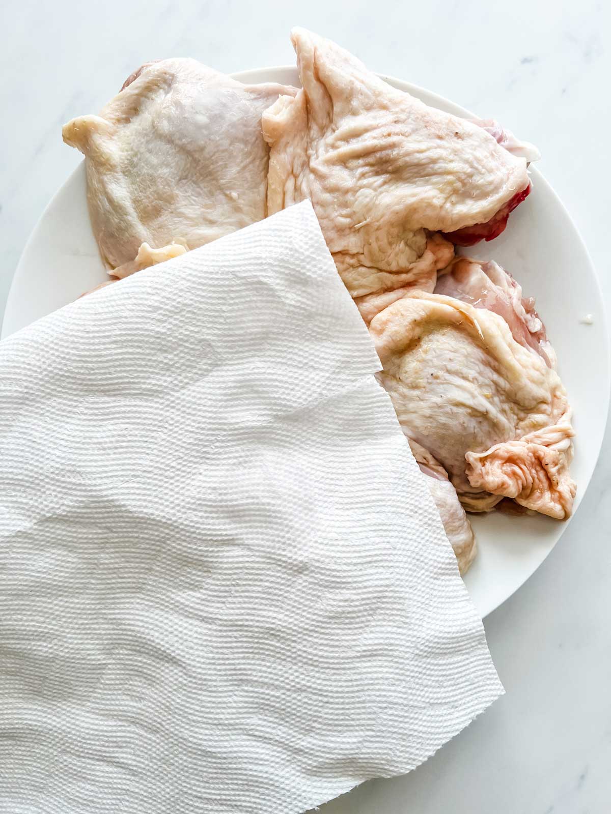 Photo of chicken thighs being dried with a paper towel.