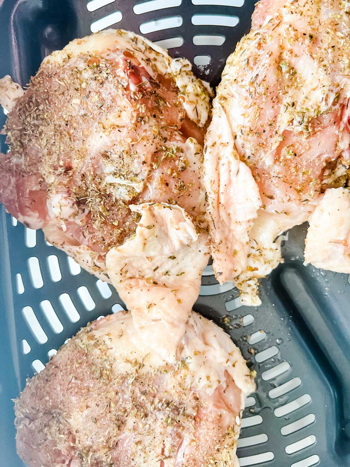 Photo of chicken thighs in an air fryer basket.