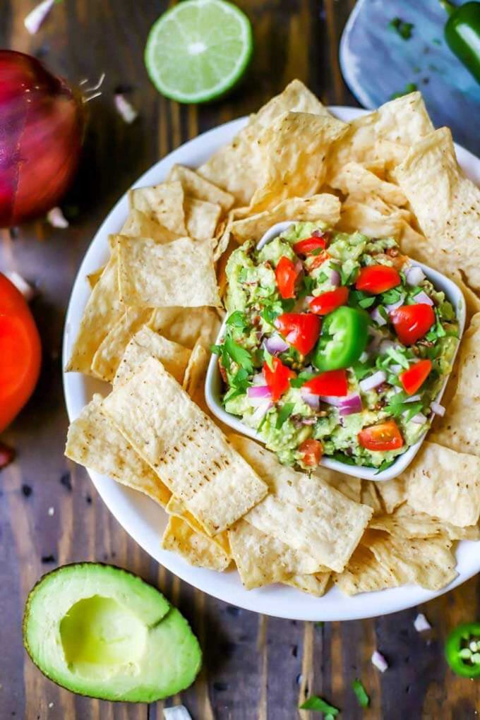 Photo of a platter of tortilla chips with a dish of guacamole in the center on a dark wooden background.