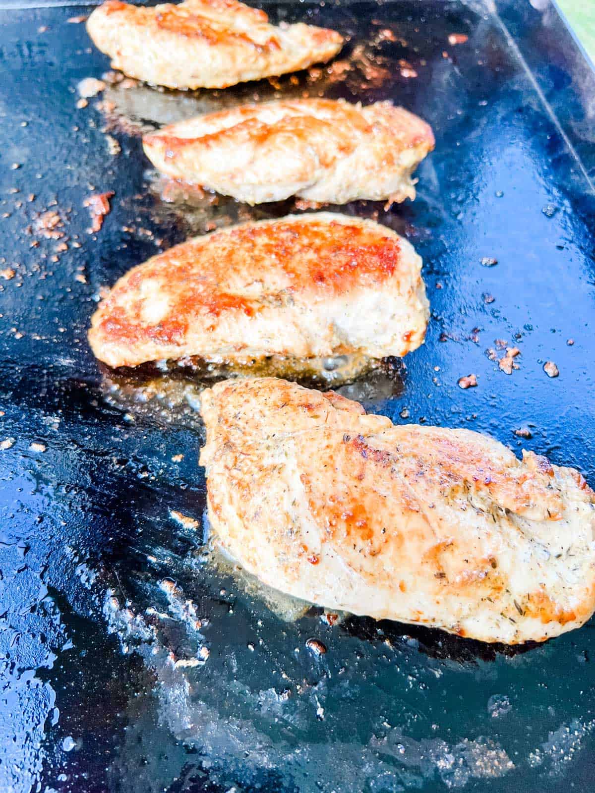 Photo of chicken that is partially cooked on a blackstone griddle.
